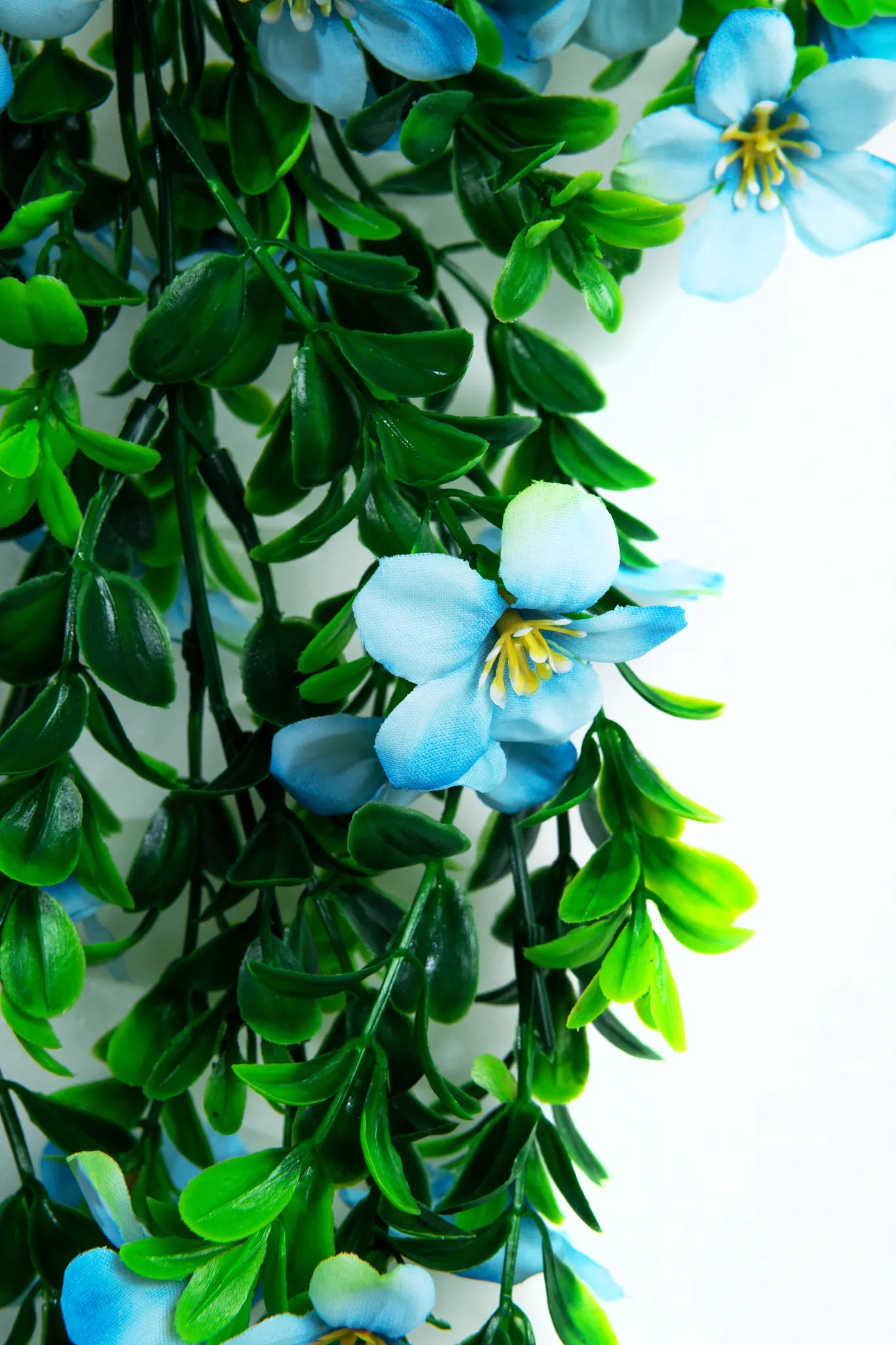 Detalle guirnalda colgante artificial con follaje verde y flores color azul claro, ideal para decorar bodas, baby showers, eventos, arcos florales y espacios interiores.