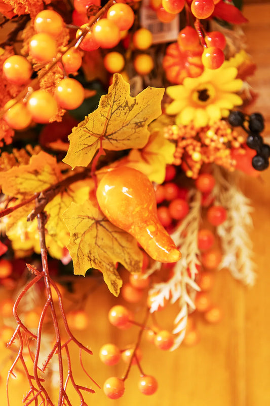 Detalle de un pick otoñal artificial con calabaza, hojas de maple, bayas y flores integrado en una corona decorativa de otoño.