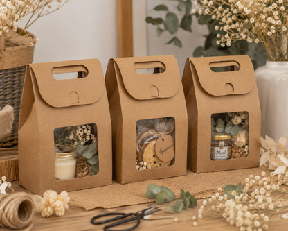 Cajas de cartón kraft con ventana transparente para regalos, recuerdos y detalles, presentadas con velas, miel, galletas y flores secas.