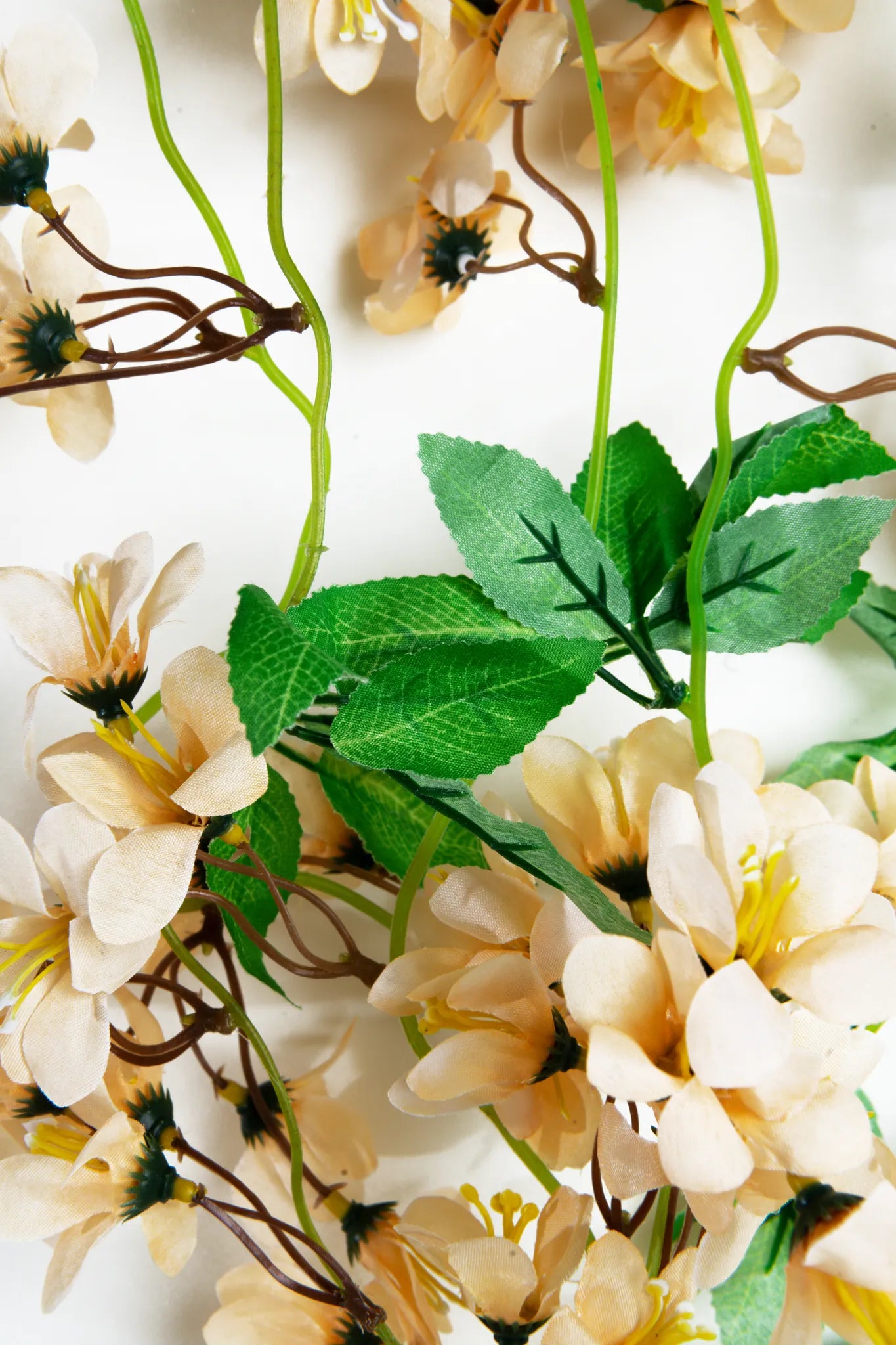Detalle guirnalda colgante artificial de flores color crema con follaje verde, ideal para decorar bodas, eventos, arcos florales, paredes y espacios interiores.