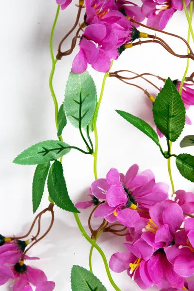 Guirnalda colgante artificial de flores moradas con follaje verde, ideal para decorar bodas, eventos, arcos florales, paredes y espacios interiores.