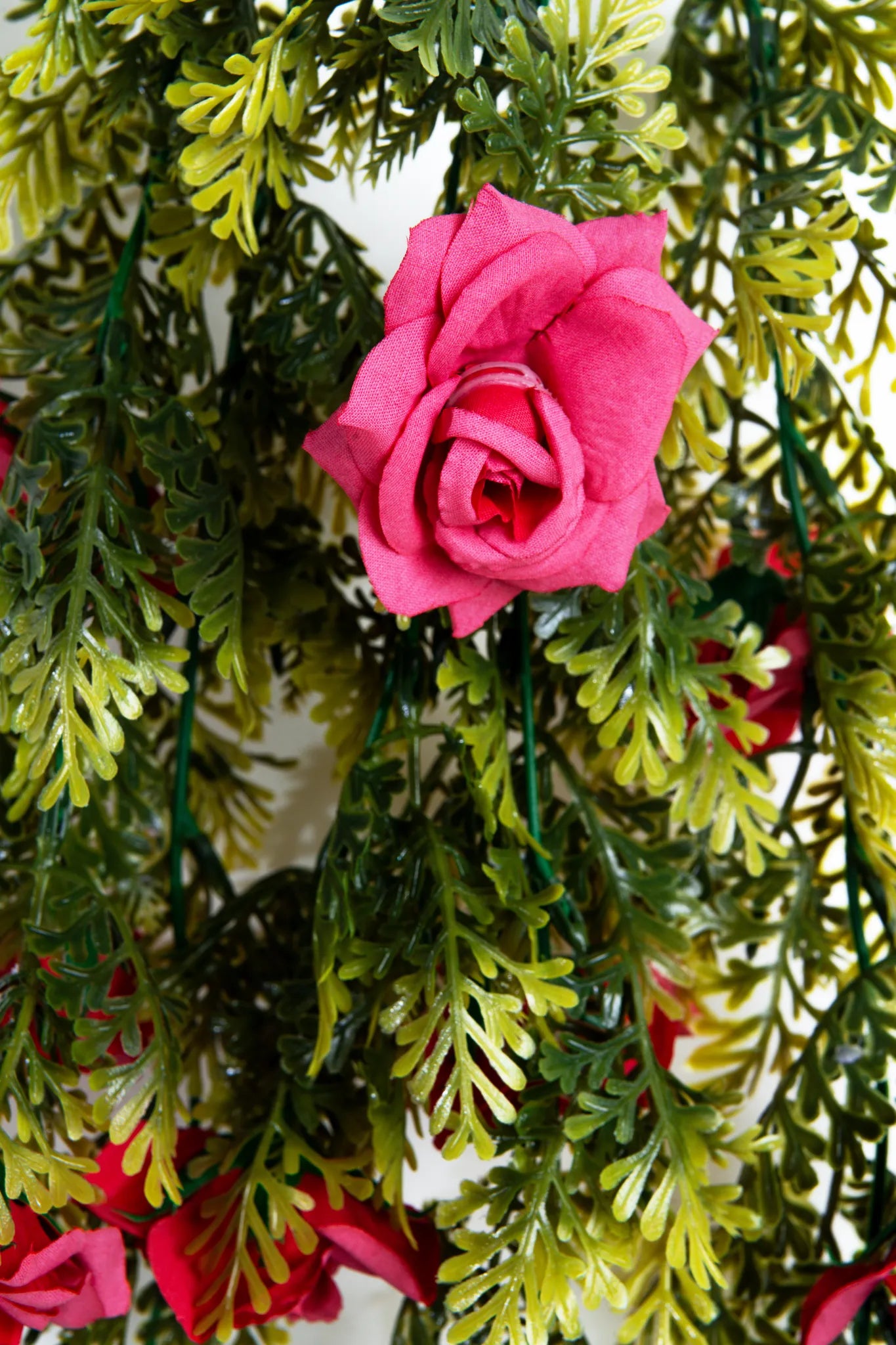 Detalle guirnalda colgante artificial con follaje verde y rosas color fucsia, ideal para decorar bodas, eventos, arcos florales, techos y espacios interiores.