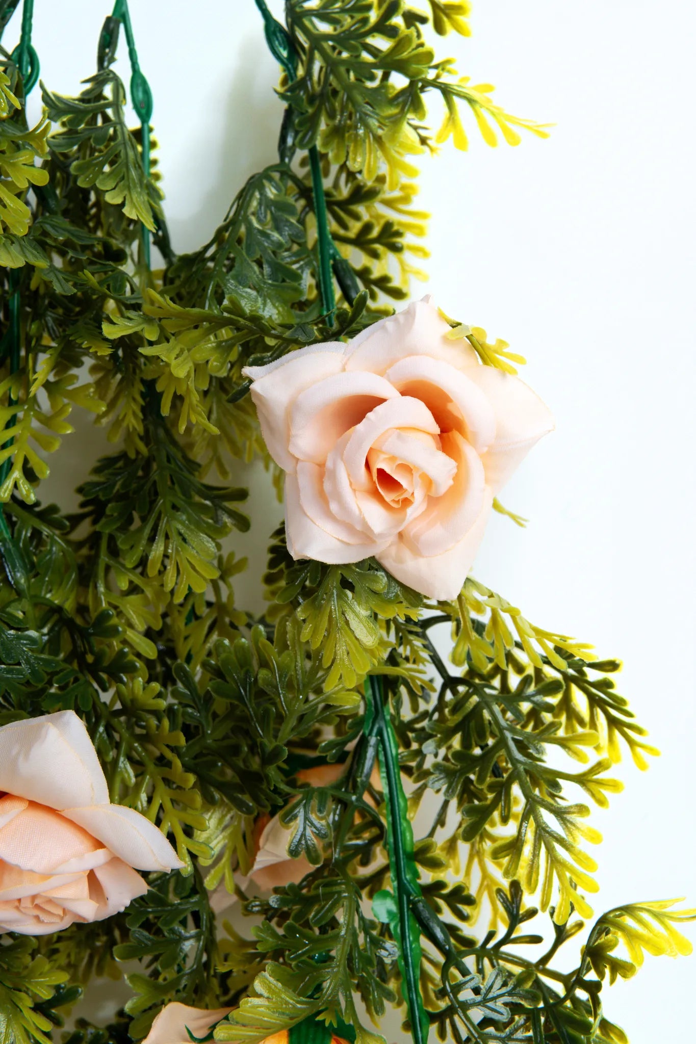 Detalle guirnalda colgante artificial con follaje verde y rosas color rosa claro, ideal para decorar bodas, eventos, arcos florales, techos y espacios interiores.