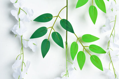 Detalle guirnalda colgante artificial de wisteria blanca con hojas verdes y flores en cascada, ideal para decorar bodas, eventos, pérgolas, arcos florales, muros verdes y espacios interiores.