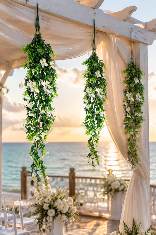 Guirnaldas colgantes artificiales con flores blancas decorando un arco para ceremonia de boda frente al mar, ideales para eventos al aire libre, bodas en la playa y montajes florales elegantes.