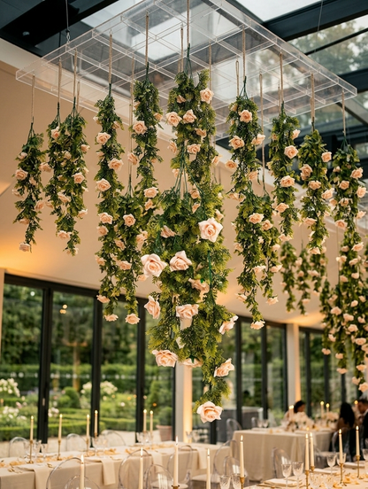 Guirnaldas colgantes artificiales con follaje verde y flores color rosa claro suspendidas del techo en la decoración de una recepción de boda, ideales para eventos, salones y montajes florales elegantes.