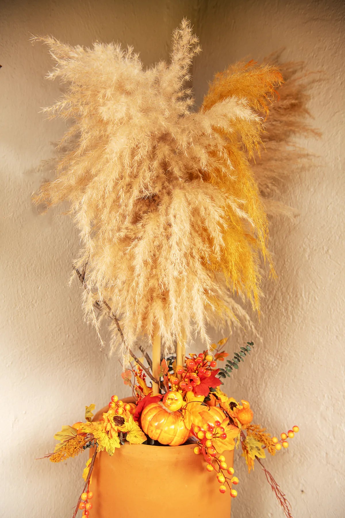 Arreglo decorativo con pampas, picks artificiales de girasol, frutos rojos y calabazas en maceta de estilo otoñal.