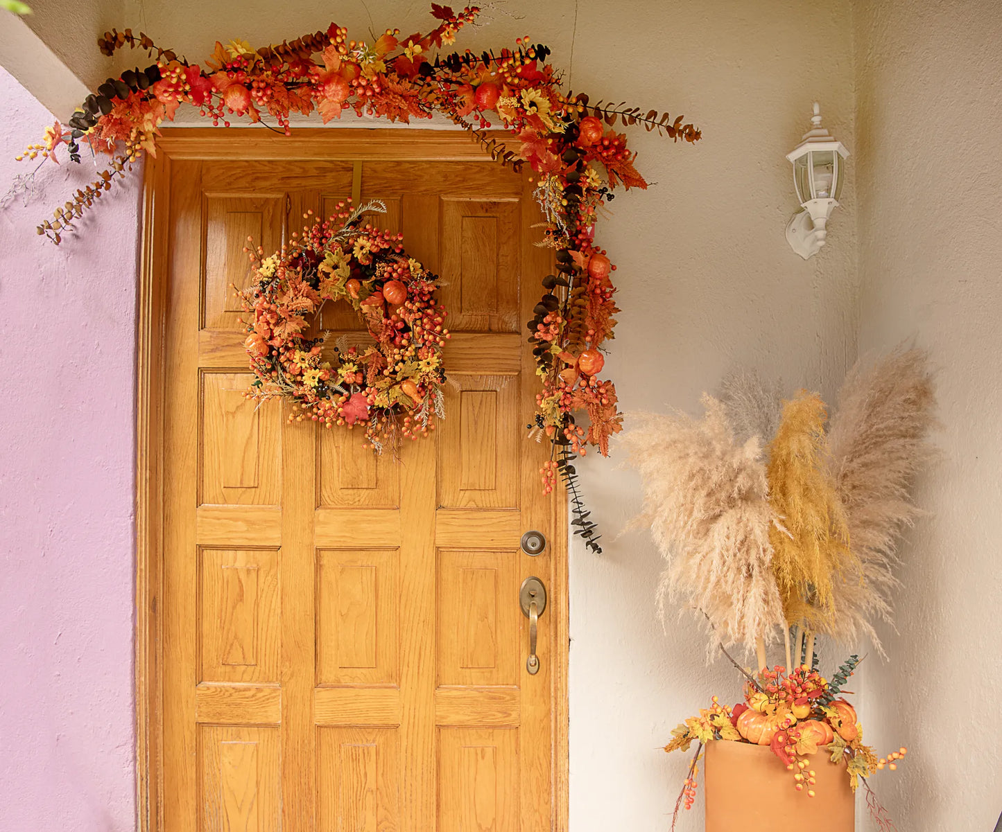 Entrada decorada con guirnalda, corona y arreglo de piso elaborados con picks artificiales de calabaza, pera, hojas otoñales y frutos decorativos.
