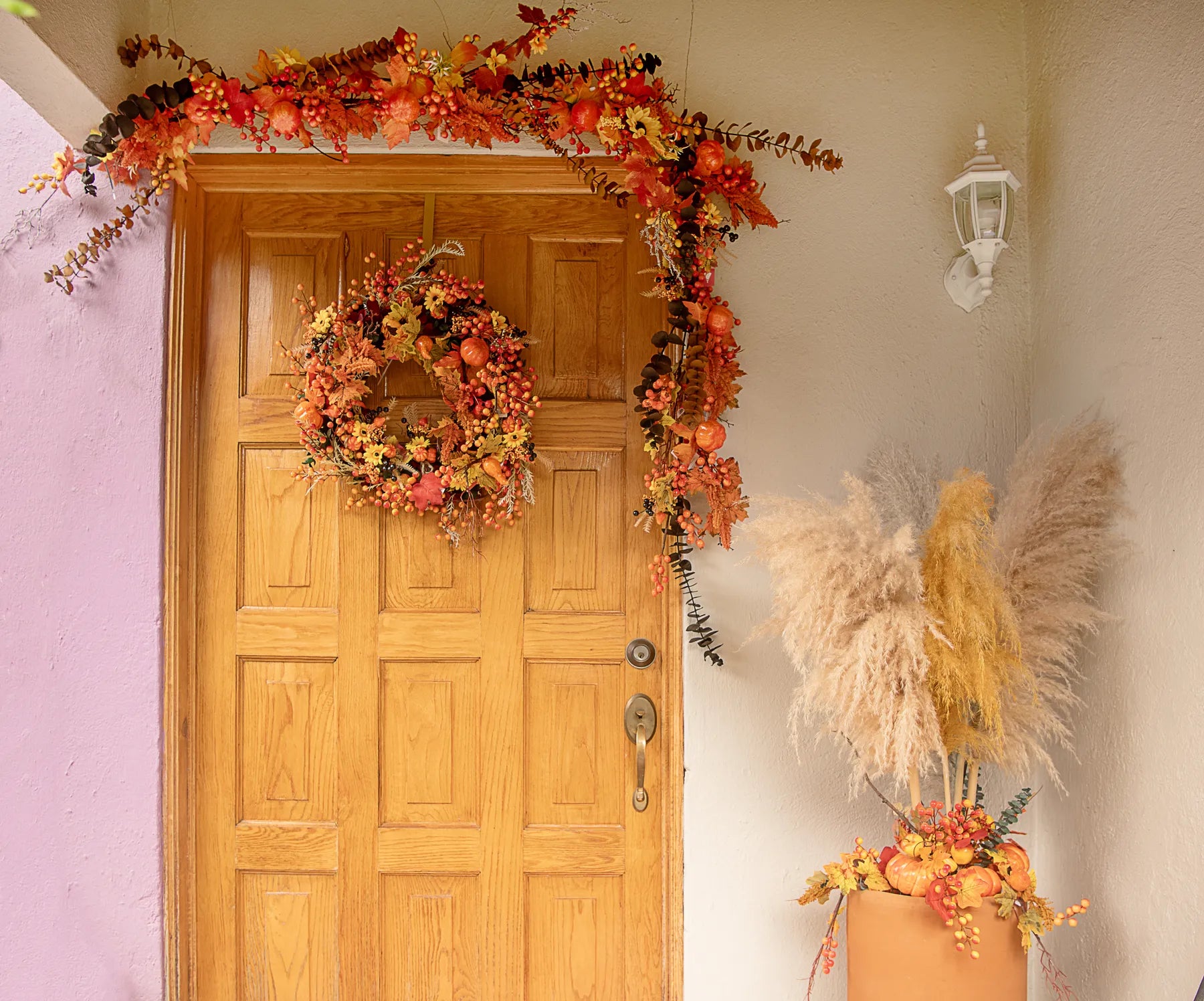 Entrada decorada con guirnalda, corona y arreglo de piso elaborados con picks artificiales de calabaza, pera, hojas otoñales y frutos decorativos.