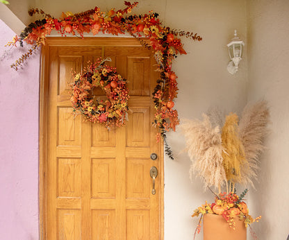 Entrada decorada con guirnalda, corona y arreglo de piso elaborados con picks artificiales de calabaza, pera, hojas otoñales y frutos decorativos.