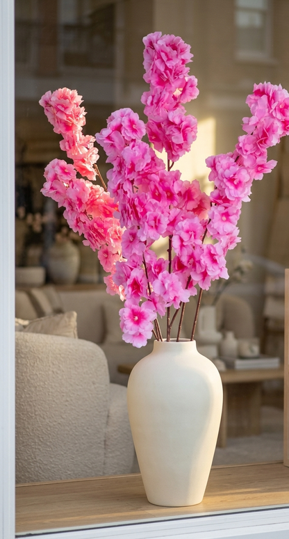Vara de cerezo artificial color rosa fucsia colocada en un florero de cerámica sobre una consola decorativa, ideal para dar un toque elegante y primaveral a la sala o recibidor.